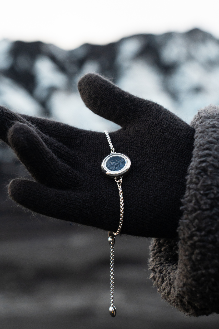 Hand wearing a black glove holding a Dragon Glass bracelet, made and designed by Lava Show against a blurred natural background