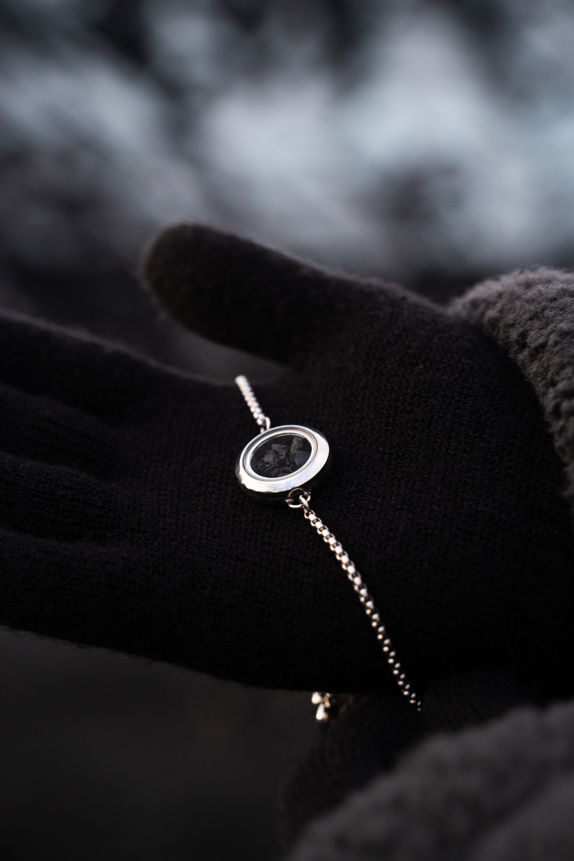 Hand wearing a black glove holding a Dragon Glass necklace with a pendant filled with obsidian against a blurred natural background.