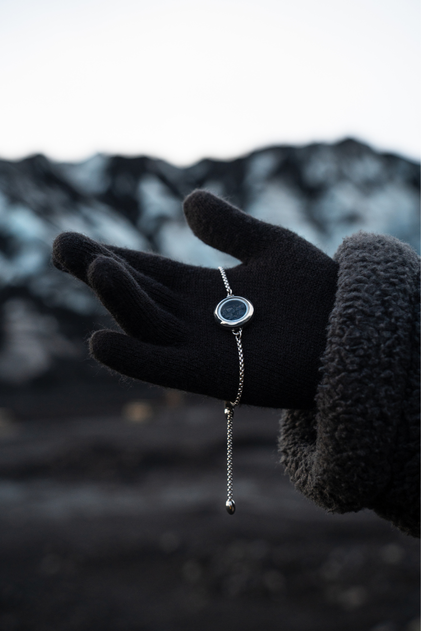 Hand wearing a black glove holding a Dragon Glass necklace with a pendant filled with obsidian against a blurred natural background