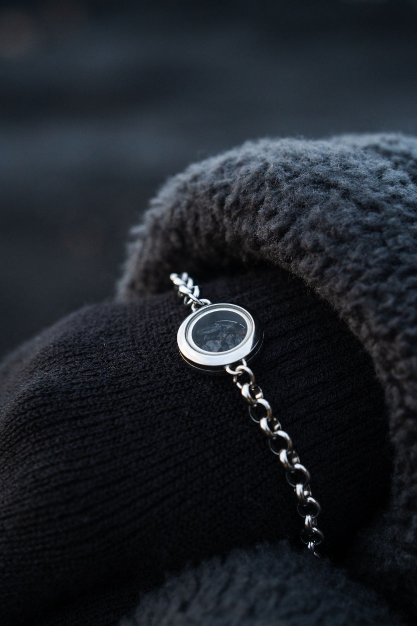 Hand wearing a black glove holding a Dragon Glass necklace with a pendant filled with obsidian against a blurred natural background