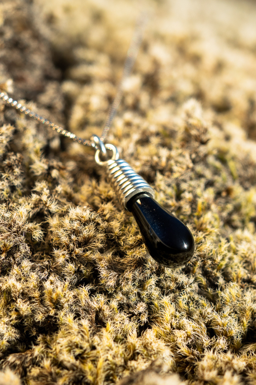Silver necklace with a black pendant on Icelandic moss.
