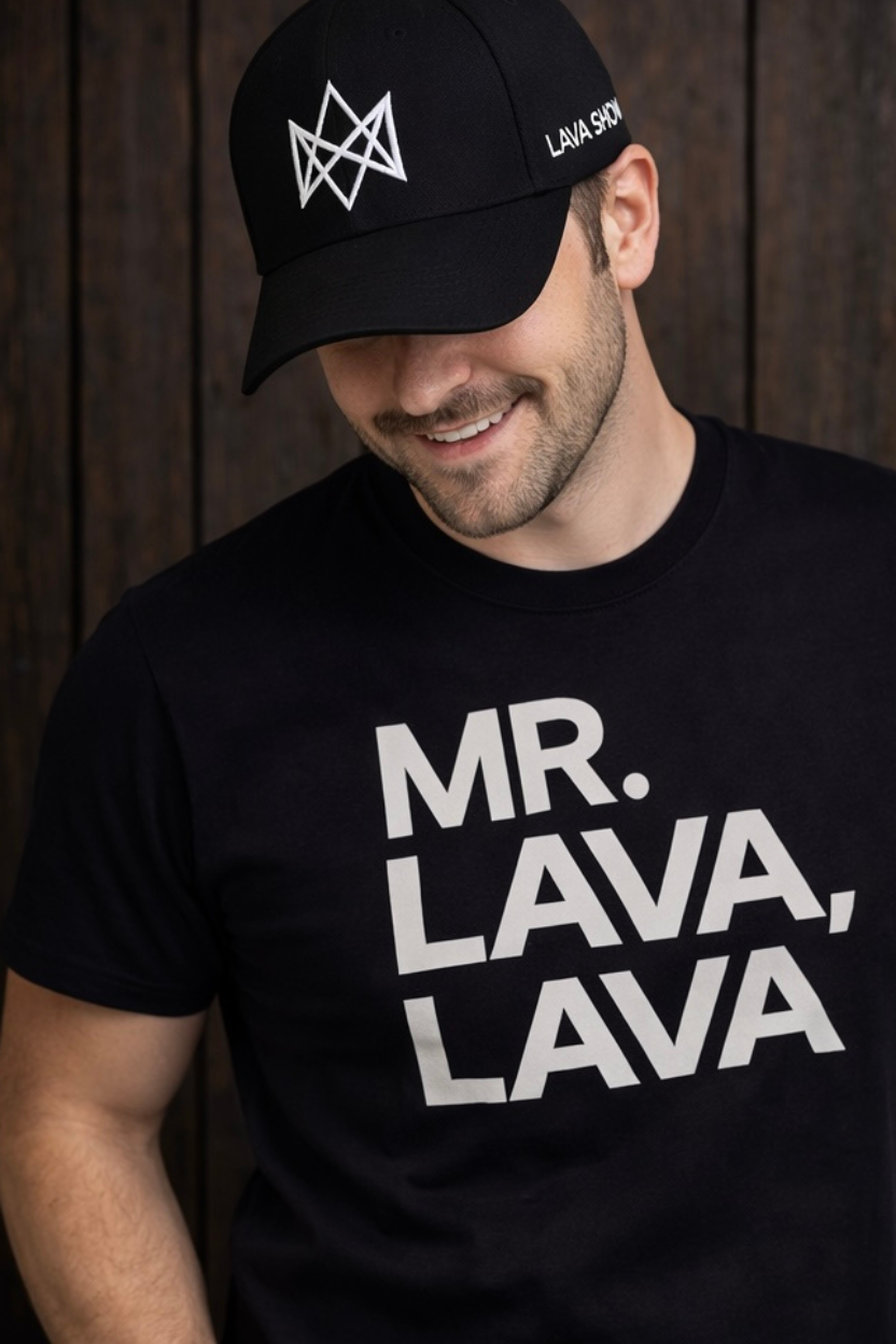 Man wearing a black cap with the Lava Show logo and t-shirt with 'MR. LAVA, LAVA' text against a wooden background